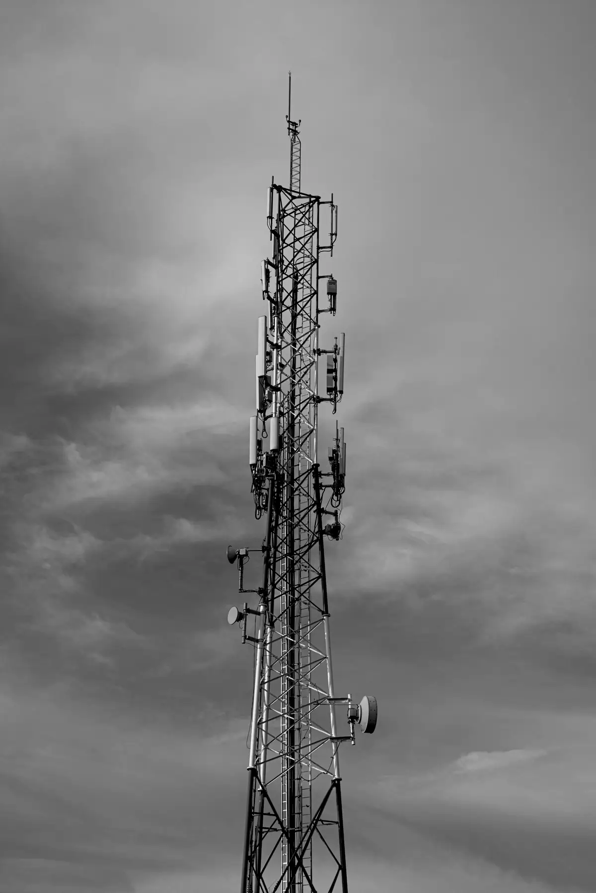 A communications tower carrying antenna panels against a cloudy sky
