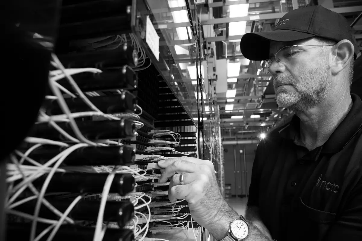 A technician in a cap inspecting fiber connections on a patch panel in an equipment room
